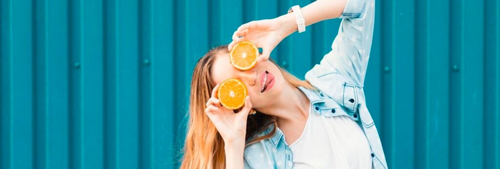 garota jovem em frente de muro azul com laranjas nos olhos fazendo careta