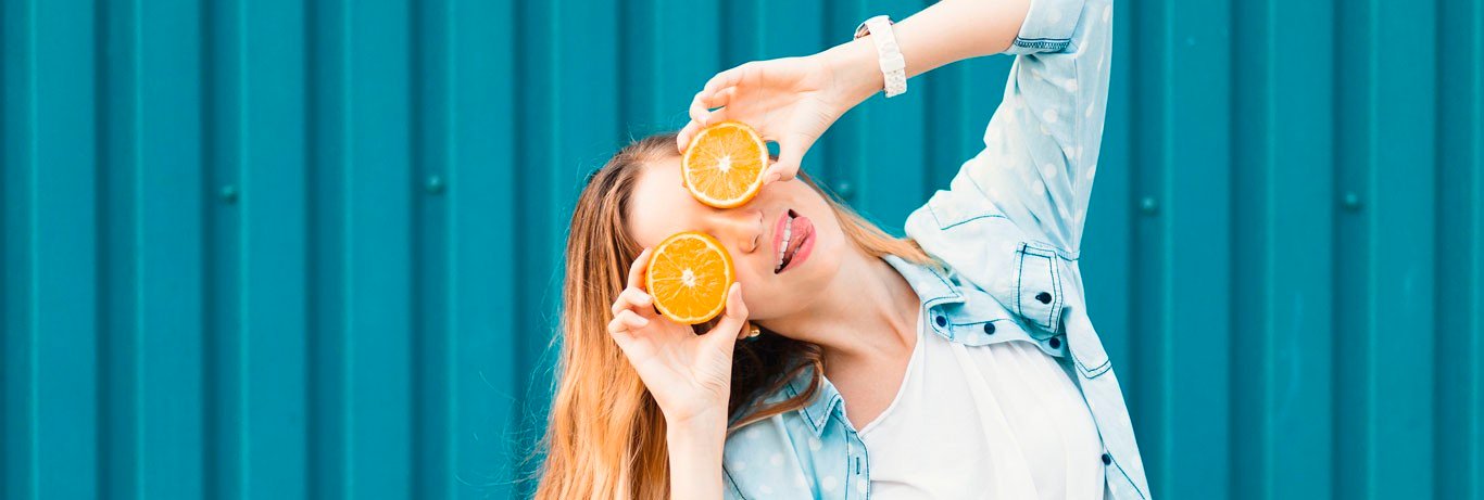 garota jovem em frente de muro azul com laranjas nos olhos fazendo careta